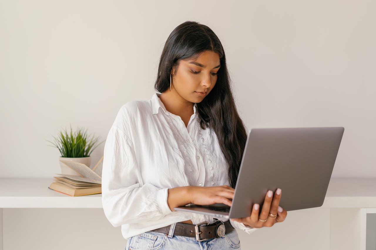 A young woman typing on a laptop while standing indoors, focused and professional.