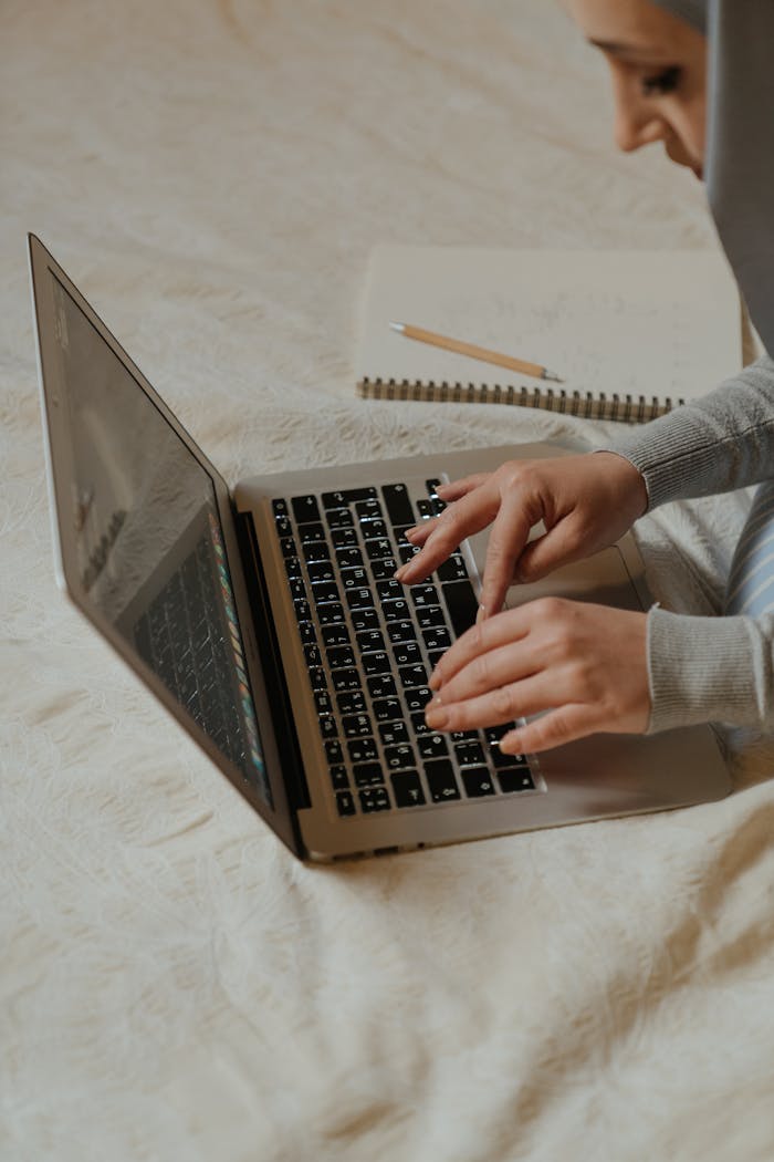 Muslim woman typing on a laptop indoors, engaging in remote work, education, or online activities.
