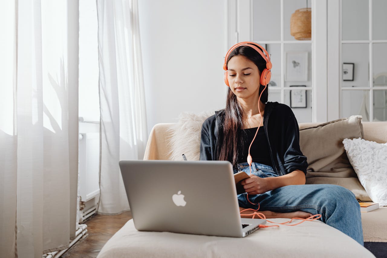 Teenage girl wearing headphones using a laptop for online learning at home in a cozy setting.